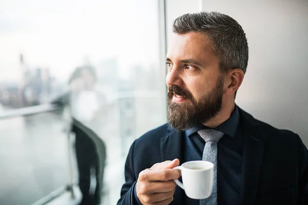 Portrait d'un homme d'affaires avec une tasse de café regardant par la fenêtre d'un bureau . — Photo