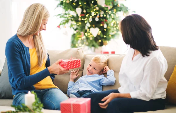 Una madre y una abuela dando regalos a un niño pequeño en casa en Navidad . — Foto de Stock