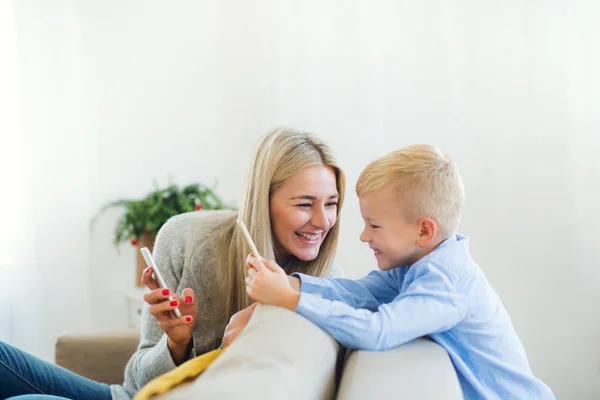 Egy anya és a kisfiú ül a kanapén, otthon karácsonykor okostelefonok. — Stock Fotó