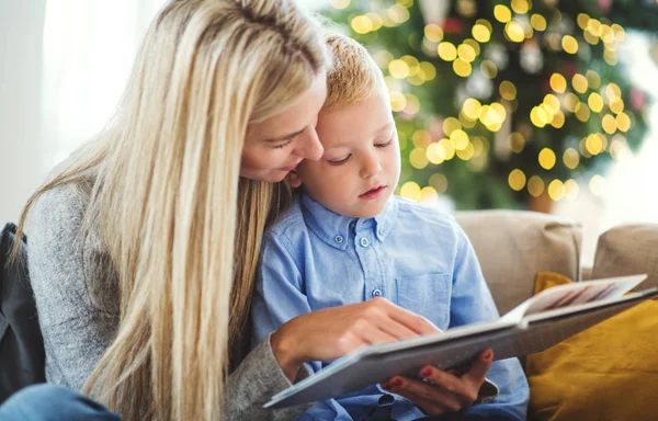 一个母亲和小男孩坐在沙发上在家里在圣诞节的时候, 读一本书. — 图库照片