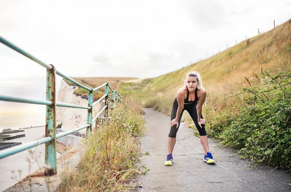 Giovane donna sportiva corridore in activewear nero in piedi fuori dal mare, a riposo . — Foto Stock