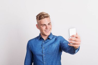 Mutlu bir genç adam selfie alarak bir stüdyoda bir akıllı telefon ile portresi.