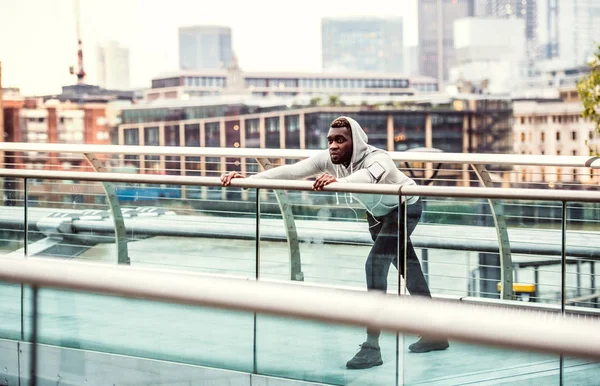 黑色男子赛跑者与智能手机在一个城市的桥梁臂章, 伸展. — 图库照片