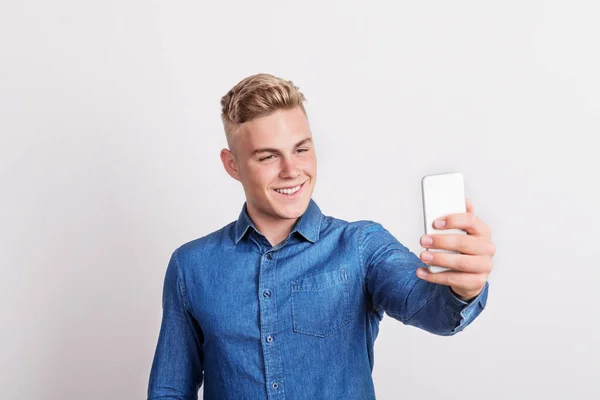 Retrato de um jovem feliz com um smartphone em um estúdio, tirando selfie . — Fotografia de Stock