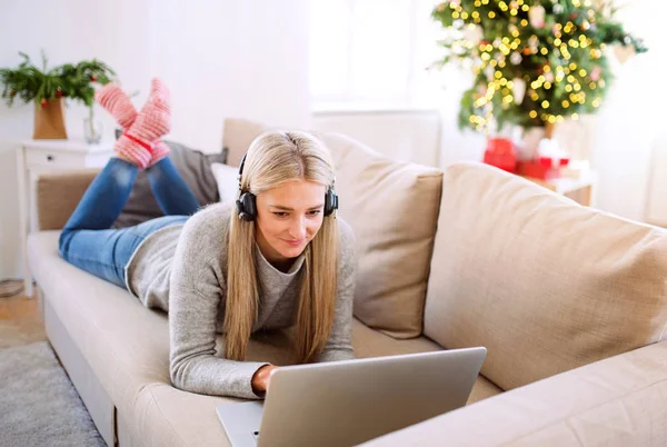 Una giovane donna con cuffie e laptop a casa nel periodo natalizio . — Foto Stock