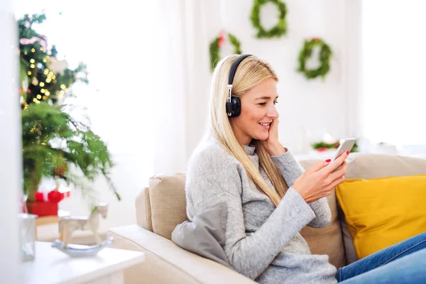 Eine junge Frau mit Kopfhörer und Smartphone zu Weihnachten zu Hause. — Stockfoto