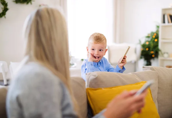 Mutter und kleiner Junge mit Smartphones sitzen zur Weihnachtszeit zu Hause auf dem Sofa. — Stockfoto