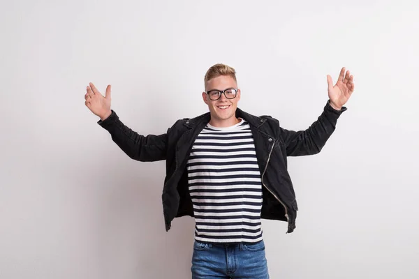 Un jeune homme confiant avec des lunettes dans un studio, portant un T-shirt rayé, les bras levés . — Photo