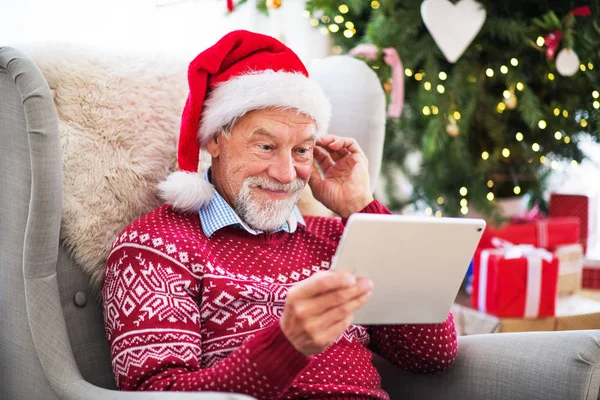 Portret starszego mężczyzny z tabletu, siedząc na fotelu w domu w czasie świąt Bożego Narodzenia. — Zdjęcie stockowe
