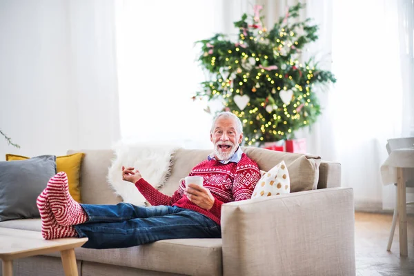 Een senior man met een kopje koffie thuis bij Kerstmis. — Stockfoto