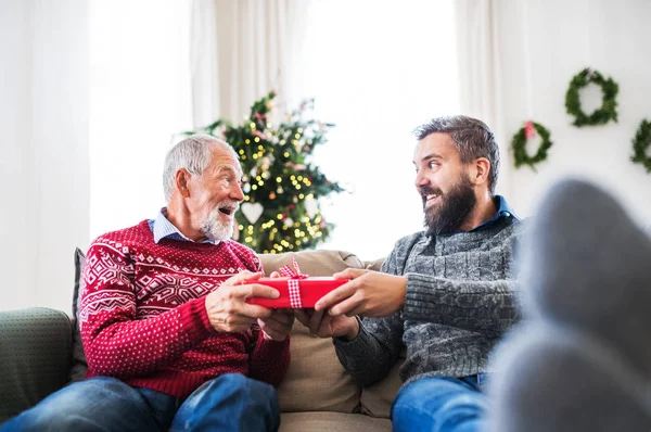 Старший батько і дорослий син з подарунком сидить на дивані в різдвяний час . — стокове фото