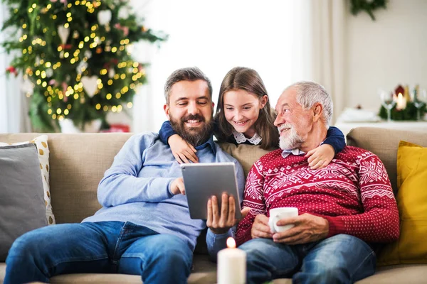 Menina pequena e seu pai e avô sentados em um sofá no Natal, usando tablet . — Fotografia de Stock