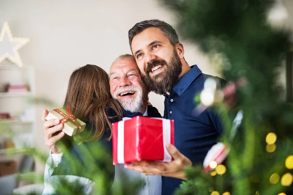 En liten flicka med far och farfar utbyta presenterar i juletid. — Stockfoto
