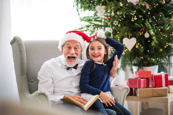 Malá holčička a její dědeček s Santa čepice a kniha v době Vánoc. — Stock fotografie