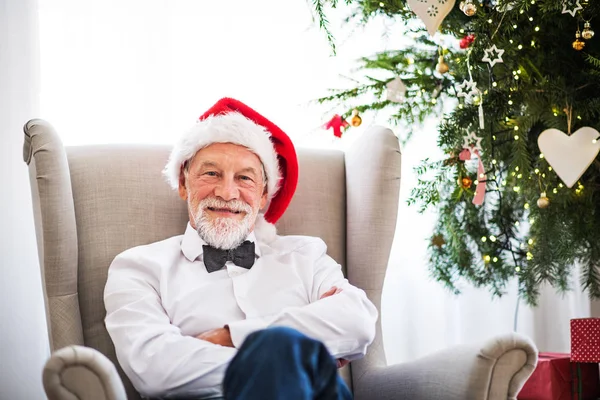 A senior man with a Santa hat at home at Christmas time. — Stock Photo, Image