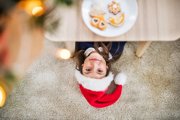 Une vue de dessus d'une petite fille avec le chapeau de Père Noël couché sur le sol à la période de Noël . — Photo