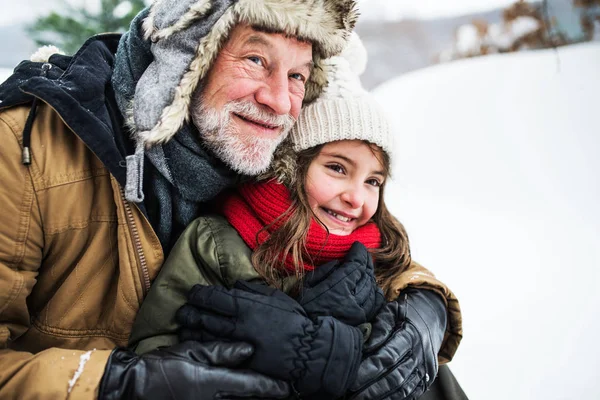 Un retrato del abuelo mayor y una niña pequeña en la nieve en un día de invierno . —  Fotos de Stock