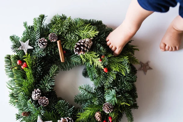 Los pies de un bebé pisando la corona de Navidad sobre un fondo blanco . — Foto de Stock