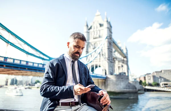 Hipster işadamı ile Tower Bridge Londra'nın başına oturmuş smartphone. — Stok fotoğraf