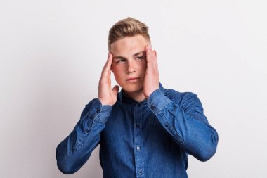 Baş ağrısı olan genç bir adam bir stüdyoda portresi.