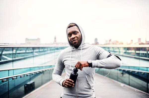 Egy fiatal sportos fekete férfi futó vizes palackot a városban. — Stock Fotó