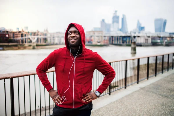 A close-up of black man runner with earphones and hood on his head in a city. Copy space.