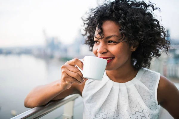 A portrait of a woman standing on a terrace, drinking coffee. — Stock Photo, Image