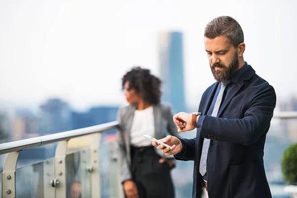 Um retrato de um homem de negócios com smartphone em pé em um terraço . — Fotografia de Stock