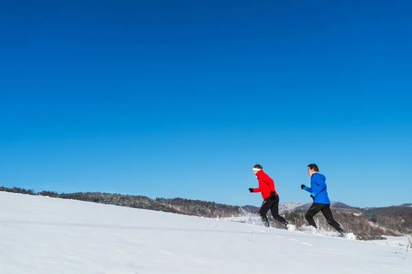 Eine Seitenansicht eines älteren Paares beim Joggen in verschneiter Winternatur. Kopierraum. — Stockfoto