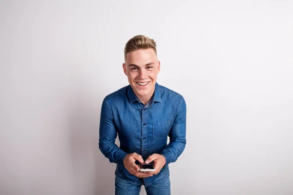 Retrato de un joven feliz en un estudio, sosteniendo un smartphone . — Foto de Stock