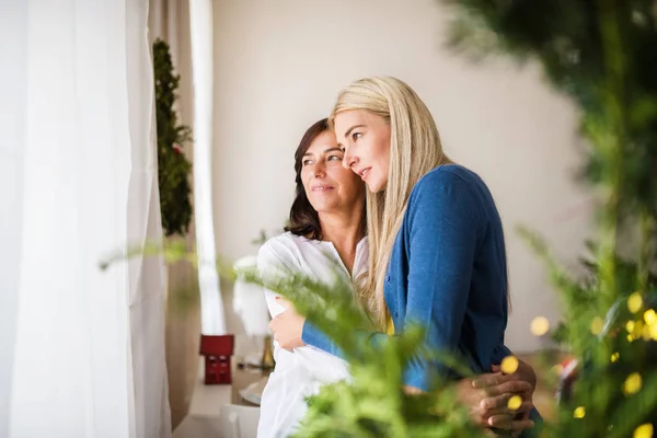 Senior woman with adult daughter at home at Christmas time, hugging. — Stock Photo, Image