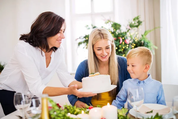 Un petit garçon avec sa mère regardant grand-mère mettre un gâteau sur la table à Noël . — Photo