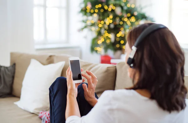 Eine Seniorin mit Kopfhörern, die zu Weihnachten zu Hause Musik hört. — Stockfoto