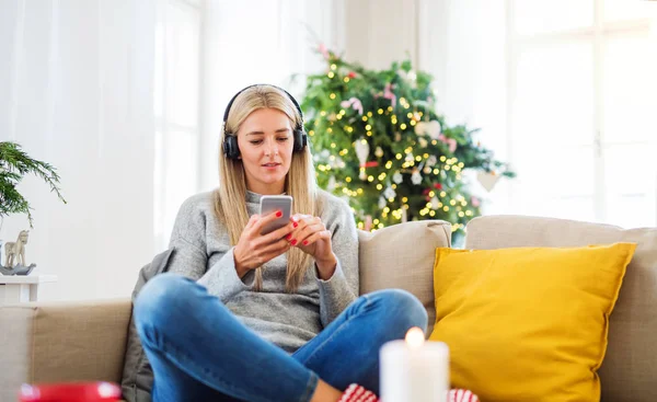 Eine junge Frau mit Kopfhörer und Smartphone zu Weihnachten zu Hause. — Stockfoto