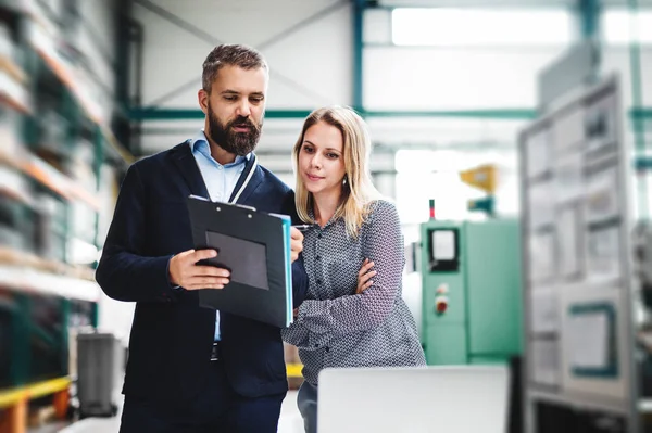 A portrait of an industrial man and woman engineer with laptop in a factory, working. — Stock Photo, Image