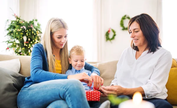 Um menino pequeno com mãe e avó presente de abertura em casa na época do Natal . — Fotografia de Stock