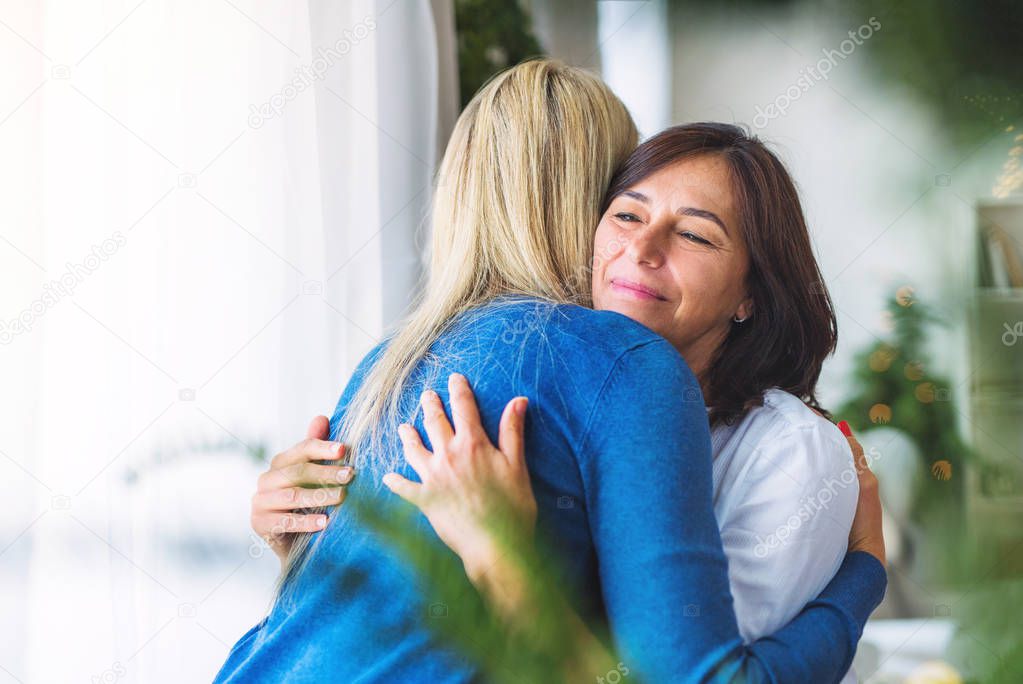 Senior woman with adult daughter at home at Christmas time, hugging.