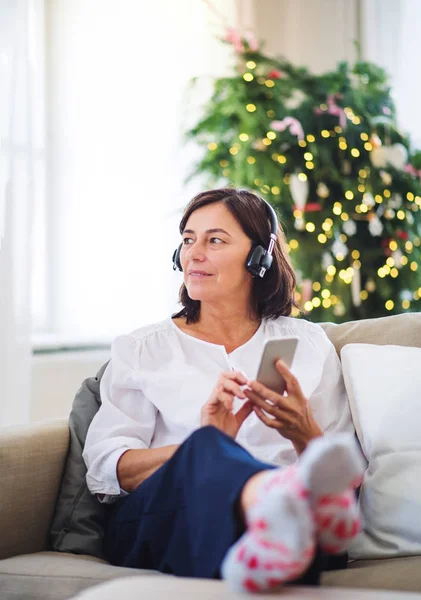 Старша жінка з навушниками, що слухають музику вдома в різдвяний час . — стокове фото