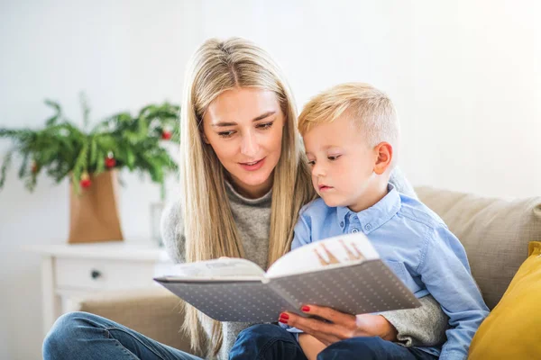 Een moeder en een kleine jongen zat op een sofa thuis bij Kerstmis, een boek lezen. — Stockfoto