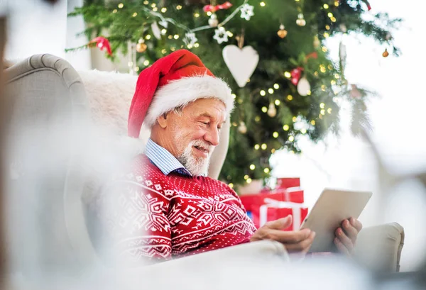 Um retrato de homem sênior com tablet sentado em poltrona em casa na época do Natal . — Fotografia de Stock