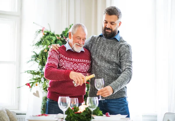 Um pai sênior e um filho adulto derramando vinho em um copo na época do Natal . — Fotografia de Stock