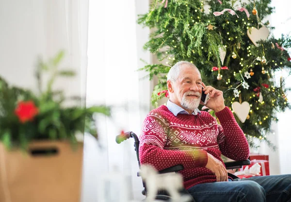 Een senior man in rolstoel met mobiele telefoon thuis tegen Kersttijd maken een telefoongesprek. — Stockfoto