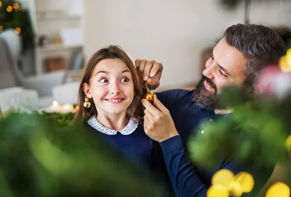 Small girl standing by a Christmas tree with her father at home, having fun. — Stock Photo, Image