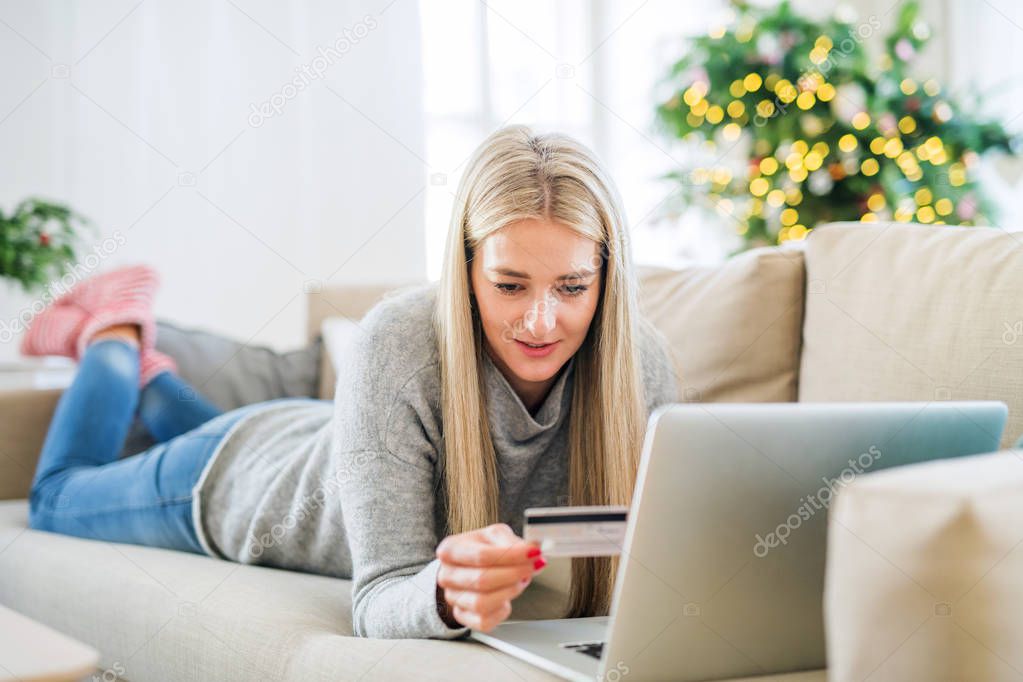 A young woman with credit card and laptop at home at Christmas time.