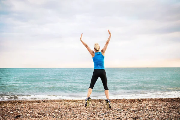 Giovane donna sportiva corridore in blu abbigliamento sportivo saltare sulla spiaggia al di fuori . — Foto Stock