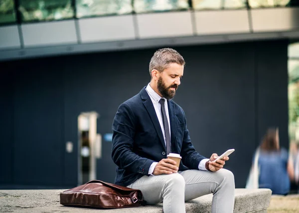 Empresário Hipster com café e smartphone sentado ao ar livre na cidade . — Fotografia de Stock