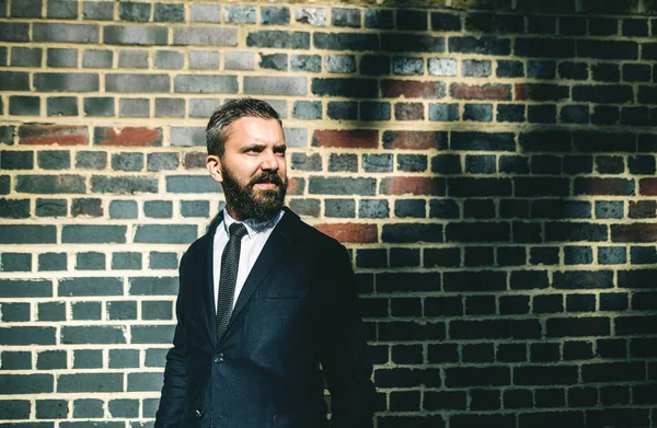Hipster businessman standing against brick wall on the street in London. — Stock Photo, Image