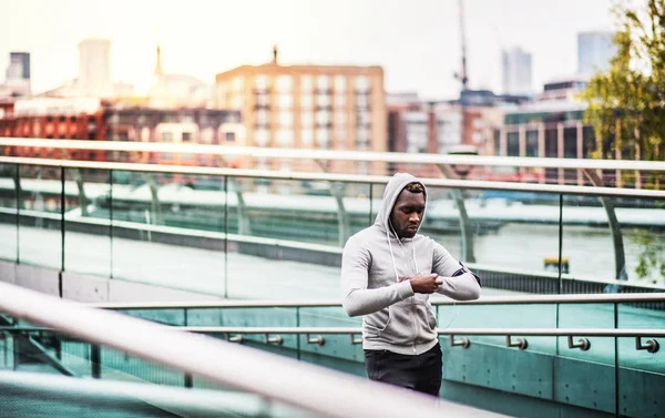 Hombre negro corredor descansando en el puente en una ciudad, comprobando la hora . —  Fotos de Stock