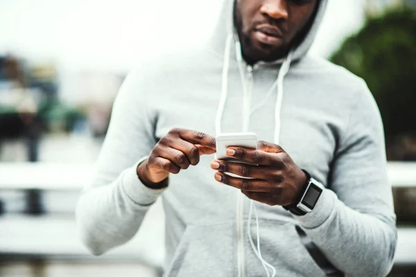 Corredor homem preto com relógio inteligente e smartphone na ponte em uma cidade, descansando . — Fotografia de Stock
