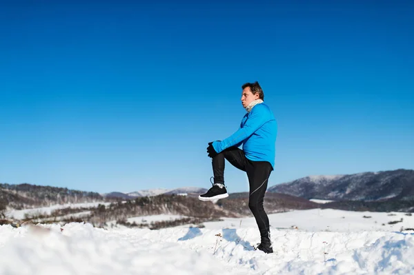 Senior man die zich uitstrekt voordat de run in de winter natuur. Kopiëren van ruimte. — Stockfoto